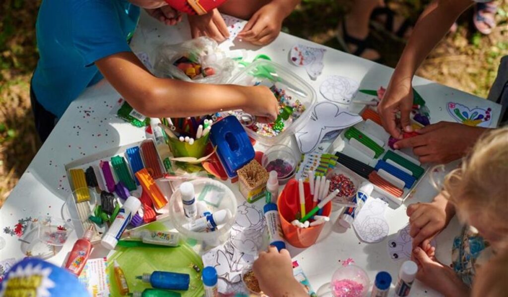 A group of children playing with craft materials areound a table.